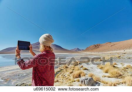 Stock Image - Woman photographing landscape, using digital tablet, Salar de Chalviri, Chalviri, Oruro, Bolivia, South America. Fotosearch