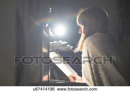 Stock Photograph - Woman reading at desk by table lamp. Fotosearch