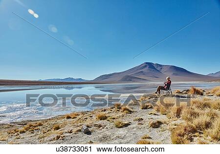 Stock Image - Woman sitting in camping chair, looking at view, Salar de Chalviri, Chalviri, Oruro, Bolivia, South America. Fotosearch