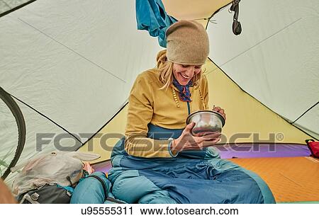 Stock Image - Woman sitting in tent, eating food from bowl, Ventilla, La Paz, Bolivia, South America. Fotosearch
