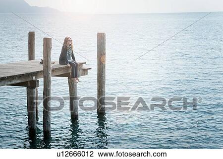 Stock Image - Woman sitting on pier looking away. Fotosearch