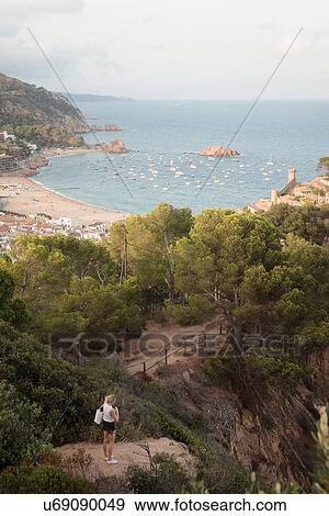 Stock Photo - Woman standing on rock, looking at view, elevated view, Tossa de mar, Catalonia, Spain. Fotosearch