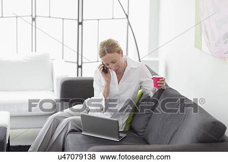Woman talking on phone and using laptop in living room View Large Photo Image Stock Photo - Woman talking on phone and using laptop in living room. Fotosearch