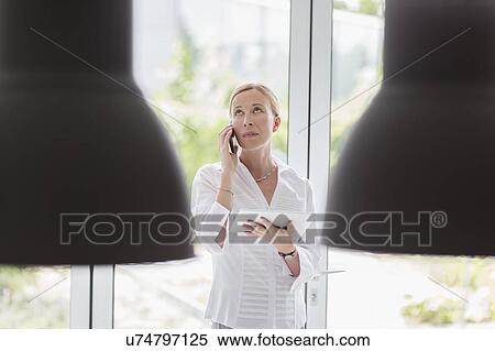 Stock Photography - Woman talking on phone and using digital tablet. Fotosearch