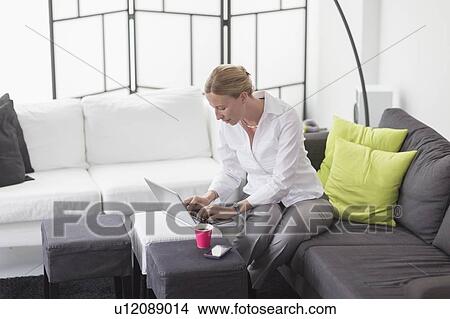 Picture - Woman using laptop in living room. Fotosearch