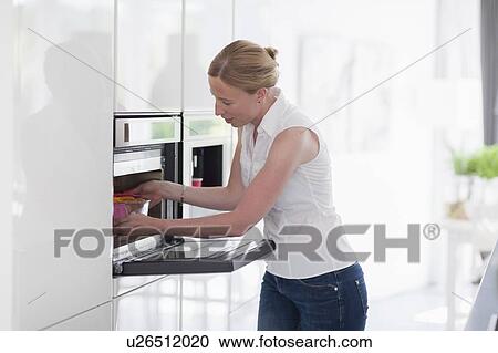 Stock Image - Woman using oven in kitchen. Fotosearch