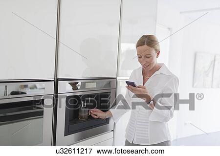 Stock Photo - Woman using phone in kitchen. Fotosearch
