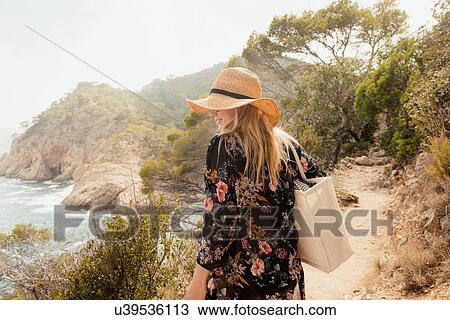 Stock Image - Woman walking along coastal pathway, rear view, Tossa de mar, Catalonia, Spain. Fotosearch