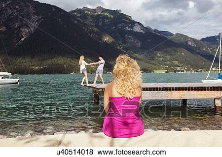 Stock Photo - Woman watching couple on pier, Achensee, Innsbruck, Tirol, Austria, Europe. Fotosearch