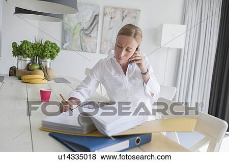 Woman working and talking on phone in dining room View Large Photo Image Stock Photo - Woman working and talking on phone in dining room. Fotosearch
