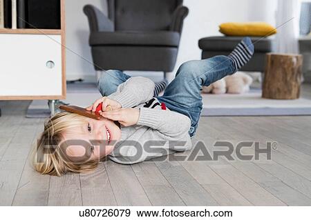 Stock Photo - Young boy lying on floor, holding smartphone to ear, smiling. Fotosearch