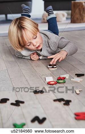 Stock Image - Young boy lying on floor, stacking magnetic letters. Fotosearch