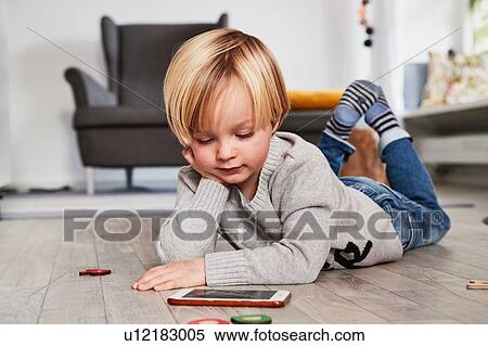 Stock Photography - Young boy lying on floor, using smartphone, looking at screen. Fotosearch