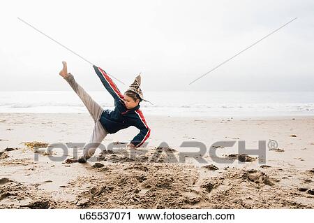 Stock Image - Young boy on beach, practising martial arts, leg raised in kick. Fotosearch