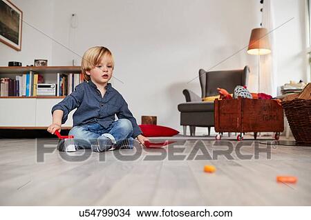Young boy sitting on floor, holding toy dustpan and brush View Large Photo Image Picture - Young boy sitting on floor, holding toy dustpan and brush. Fotosearch