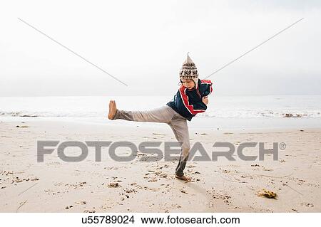 Picture - Young boy standing on beach, balancing on one leg. Fotosearch