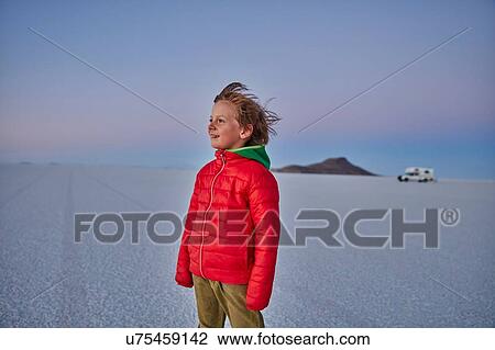 Stock Image - Young boy standing on salt flats, looking at view, recreational vehicle in background, Salar de Uyuni, Uyuni, Oruro, Bolivia, South America. Fotosearch