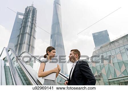 Young businessman and woman moving up escalator in Shanghai financial centre, Shanghai, China View Large Photo Image Stock Image - Young businessman and woman moving up escalator in Shanghai financial centre, Shanghai, China. Fotosearch