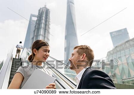 Stock Photo - Young businessman and woman moving up escalator in Shanghai financial centre, Shanghai, China. Fotosearch