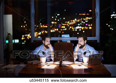 Young businessman at office desk looking at computer at night, mirror image View Large Photo Image Stock Photography - Young businessman at office desk looking at computer at night, mirror image. Fotosearch