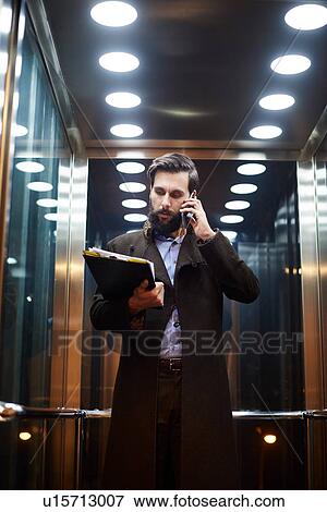 Young businessman in elevator making smartphone call View Large Photo Image Stock Photo - Young businessman in elevator making smartphone call. Fotosearch