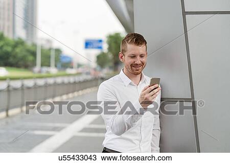 Stock Image - Young businessman looking at smartphone touchscreen in city, Shanghai, China. Fotosearch