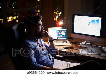 Young businessman staring at computer on office desk at night View Large Photo Image Stock Photo - Young businessman staring at computer on office desk at night. Fotosearch