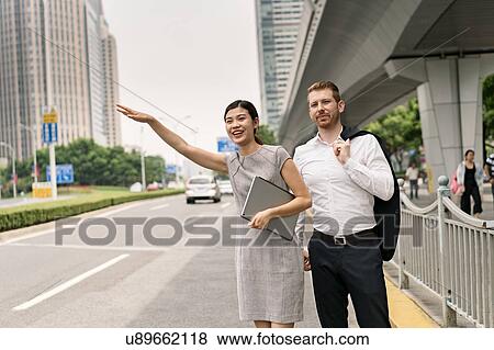 Stock Photo - Young businesswoman and man hailing a taxi in city, Shanghai, China. Fotosearch