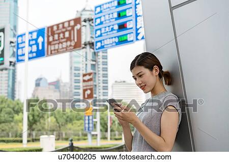 Stock Photography - Young businesswoman looking at smartphone in city, Shanghai, China. Fotosearch