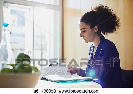 Stock Image - Young businesswoman reading paperwork at office desk. Fotosearch