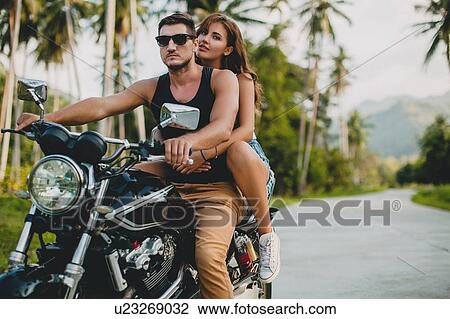 Stock Image - Young couple riding on motorcycle on rural road, Krabi, Thailand. Fotosearch