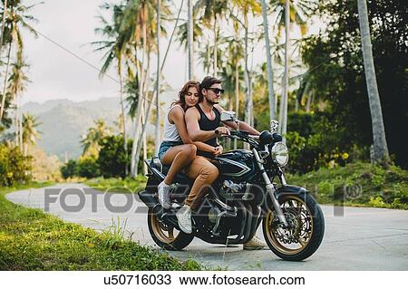 Stock Image - Young couple riding on motorcycle on rural road, Krabi, Thailand. Fotosearch