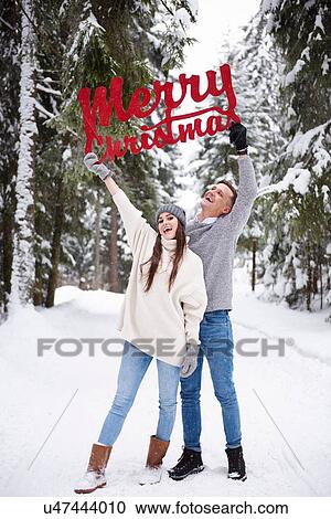 Stock Image - Young couple with Merry Christmas words in snow. Fotosearch
