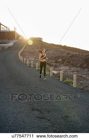 Stock Image - Young female runner running down rural road at sunset, Las Palmas, Canary Islands, Spain. Fotosearch