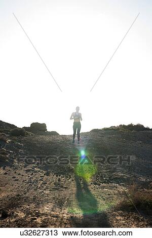 Stock Image - Young female runner running in arid landscape, Las Palmas, Canary Islands, Spain. Fotosearch
