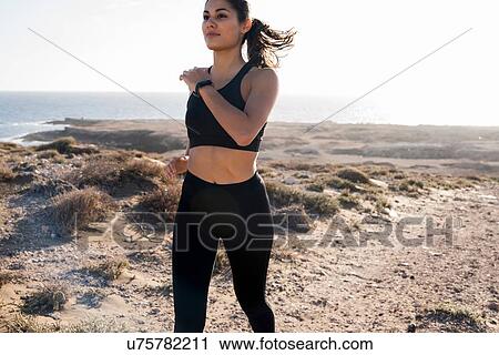 Stock Image - Young female runner running in arid coastal landscape, Las Palmas, Canary Islands, Spain. Fotosearch