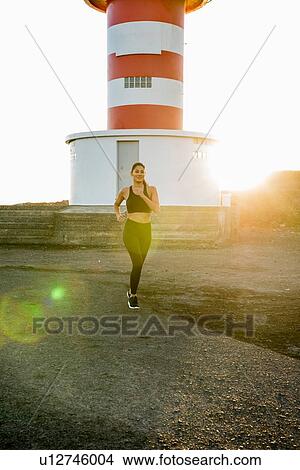 Picture - Young female runner running on coastal dirt track at sunset. Fotosearch