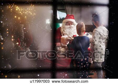 Stock Image - Young girl and boy receiving gifts from Santa, viewed through window. Fotosearch