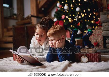 Young girl and boy relaxing beside Christmas tree, reading book View Large Photo Image Stock Photo - Young girl and boy relaxing beside Christmas tree, reading book. Fotosearch