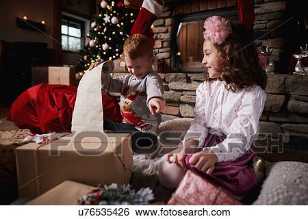 Stock Photograph - Young girl and boy sorting Christmas gifts, young boy rolling list. Fotosearch