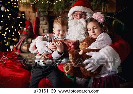 Stock Photo - Young girl and boy visiting Santa, holding gifts. Fotosearch
