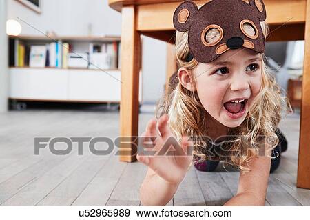 Stock Photo - Young girl crawling under table, wearing bear mask, laughing. Fotosearch