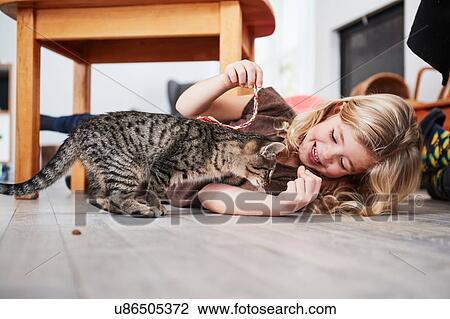 Stock Image - Young girl lying on floor, playing with pet cat. Fotosearch