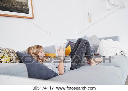 Young girl lying on sofa, reading book View Large Photo Image Stock Photo - Young girl lying on sofa, reading book. Fotosearch