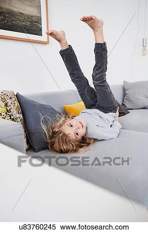 Stock Photography - Young girl lying on sofa with legs in air. Fotosearch