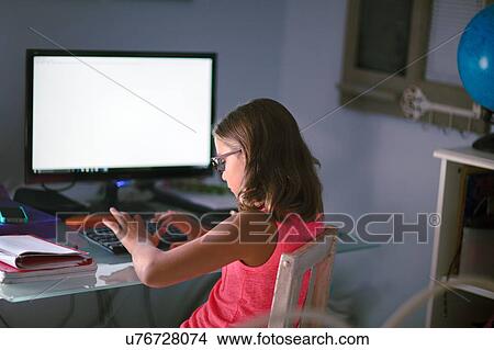 Picture - Young girl sitting at desk, doing homework, using computer. Fotosearch