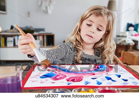 Stock Photo - Young girl sitting at table, painting picture. Fotosearch