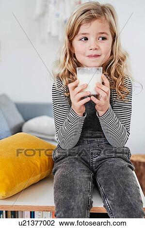 Young girl sitting in living room, holding glass of milk View Large Photo Image Stock Image - Young girl sitting in living room, holding glass of milk. Fotosearch