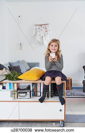 Young girl sitting in living room, holding glass of milk View Large Photo Image Stock Photo - Young girl sitting in living room, holding glass of milk. Fotosearch