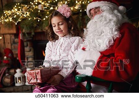 Young girl sitting with Santa, holding Christmas gift View Large Photo Image Stock Image - Young girl sitting with Santa, holding Christmas gift. Fotosearch